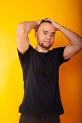 Fototapeta na wymiar a man of European appearance is very excited about holding his hands to his head against a yellow background in isolation. problems of a young guy