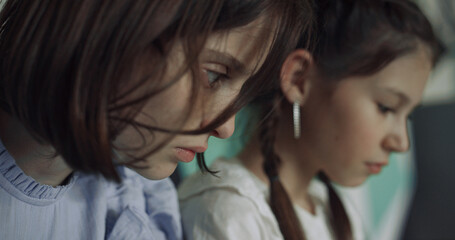 Two serious schoolgirls sitting together looking down closeup. Study concept.