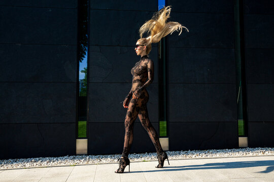 High fashion look. Glamour stylish model in black latex clothing and and high heels on is walking in the city. Sexy  blonde woman in bodystocking lingerie is posing outdoor. Sexy Lingerie model.