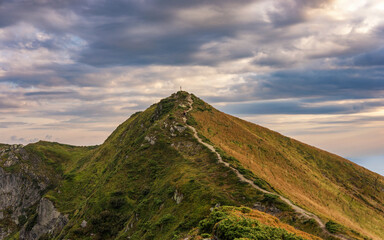 A lone man walks along a narrow path to a cross on top of a mountain. Beautiful mountain landscape with philosophical meaning