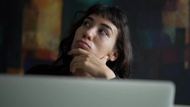One pensive hispanic woman in front of laptop. A thoughtful latin person using computer thinking of an idea