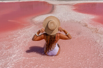 A woman traveler looks at an amazing pink salt lake. He sits with his back in a bathing suit and...