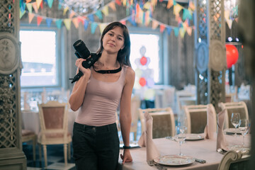 Girl photographer with a camera at work on the set in the banquet hall. A young beautiful woman - a...
