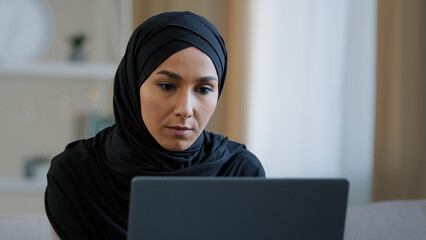 Focused ethnic female muslim arabian young woman girl islamic student businesswoman freelancer sits at home work on computer online chat search information data analyze develop web design e-commerce