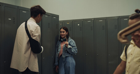 Couple joyful students talking standing at lockers lively school corridor.