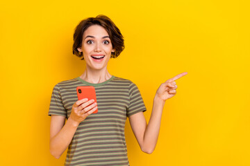 Photo of shiny excited lady wear striped t-shirt reading modern device pointing empty space isolated yellow color background