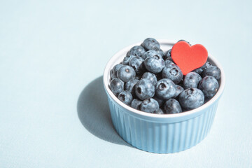 Beautiful card with red heart shape and blueberry berries in blue bowl