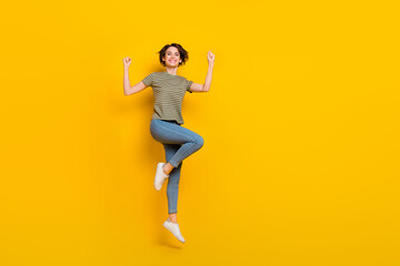 Fototapeta na wymiar Full length photo of charming lucky lady wear striped t-shirt jumping high rising fists empty space isolated yellow color background