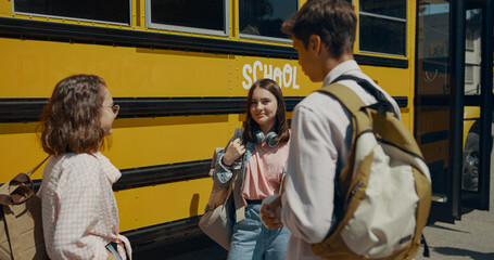 Cheerful teen classmates chatting at school bus. Friends communicating outdoors