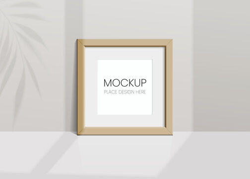 Realistic vector mockup with wooden photo frame. Shadow on the wall and empty place for your design. 3d soft light and overlay shadow from leaves of plant and window. Square poster or painting.