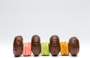 Colored donuts and macaroons placed alternately on white background. French cookies. Sweets with sugar. Colored buns and macarons.