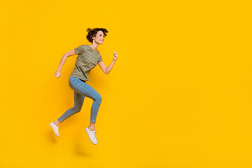 Fototapeta na wymiar Full length photo of shiny charming lady wear striped t-shirt jumping high hurrying empty space isolated yellow color background