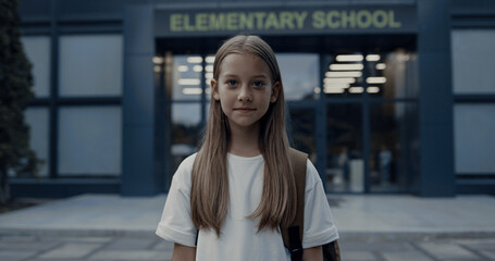 Cute shy girl standing at school entrance alone. Portrait pretty schoolgirl.