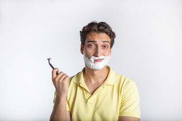 Close-up portrait photo of handsome man with a shaving foam on his face and holding razor blade...