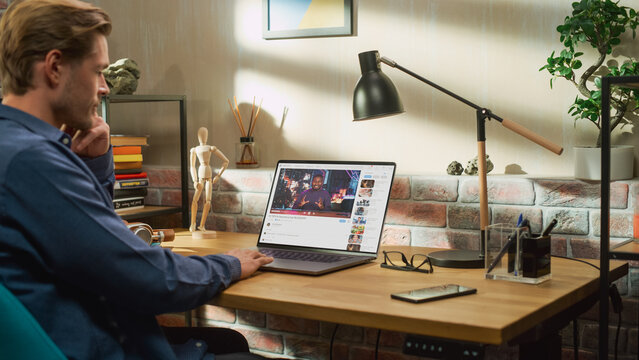 Handsome Man Using Laptop to Watch Video Sharing Service Mock-up Where African American Influencer Talks About Lifestyle. Celebrity Blogger Having fun. Interface with Related Streams, Likes, Comments.