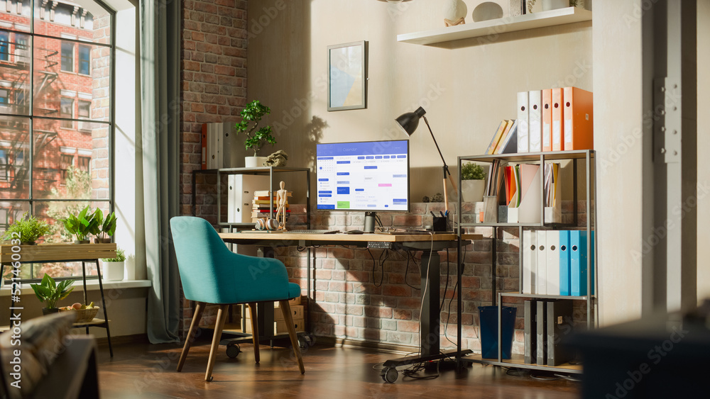 Poster Desktop Computer Monitor Standing on Height Adjustable Desk with Office Software on Display. Cozy Empty Loft Apartment with a Lamp, Notebooks and Smartphone on the Table. Home Office Concept.