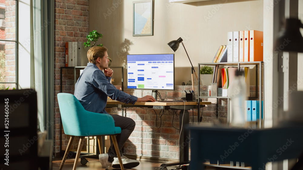Poster Remote Work Concept: Man Using Desktop Computer With Office Software to Check Schedule in Calendar. Young Male Planning Business Meetings in Stylish Loft Apartment with Big Window.