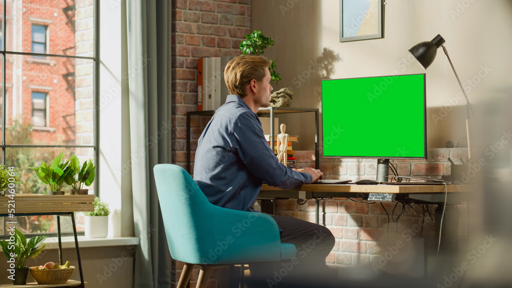 Aufkleber Young Handsome Man Working from Home on Desktop Computer with Green Screen Mock Up Display. Male Checking Corporate Accounts, Messaging Colleagues. Loft Living Room with Big Window.