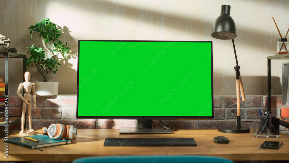 Leinwandbilder Desktop Computer Monitor Standing on a Table with a Green Screen Chromakey Mock Up Display. Cozy Empty Loft Apartment with a Lamp, Notebooks and Smartphone on the Table. Arc Shot.