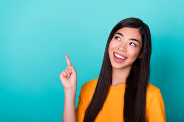 Photo of adorable cute pretty girl with long hairdo wear yellow t-shirt directing empty space beaming isolated on teal color background