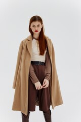 Naklejka premium A red-haired lady in a beige coat on a white background. Advertising for brands showrooms catalog of clothing for women