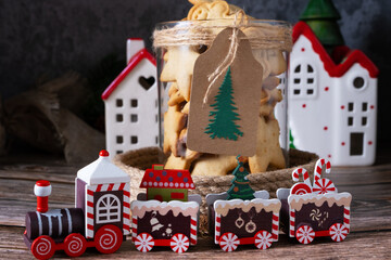 Homemade Christmas cookies in a glass jar with New Year's table decoration, next to a toy steam locomotive and houses