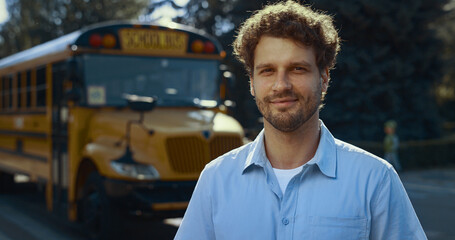 Smiling man driver posing near bus close up. Schoolbus operator looking camera.