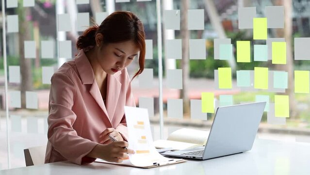 Businesswoman in bank office working with laptop and analyzing financial documents for bookkeeping.