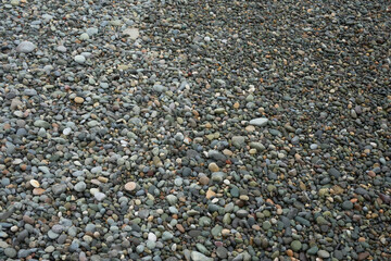 Background of wet stones on a pebble beach, natural rounded gravel on the seashore. Stone and gravel background