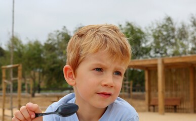 A blond boy with a spoon in his hand and his lips smeared with condensed milk. A five-year-old boy looks intently into the distance. 