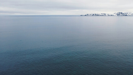 Snowy blue winter landscape of Arctic ocean and snow covered stony shore. Footage. Aerial of the coastline, cliffs, endless ocean and heavy cloudy sky on the background.