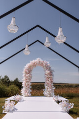 Place for wedding ceremony in garden outdoors. Wedding arch decorated with flowers and crystal chandeliers. Wedding setting.