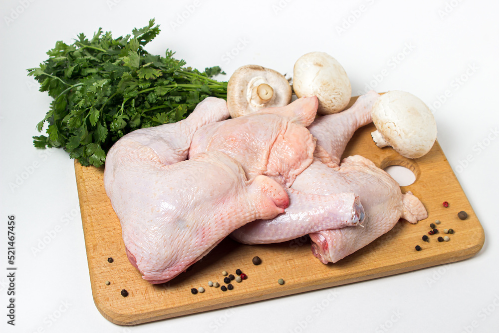 Wall mural Chicken legs isolated on white background. Chicken meat with vegetables and herbs on a wooden cutting board.