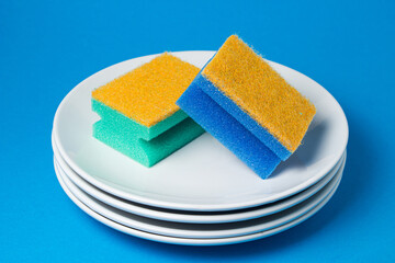 Sponges for washing dishes on on plates on a blue background. Means for cleaning and cleaning