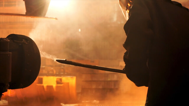 Side View Of The Perator Remove Waste From Furnace Pipe At The Iron Melting Plant. Stock Footage. Man Worker In Heat Resistant Suit Cleaning High Temperature Furnace.