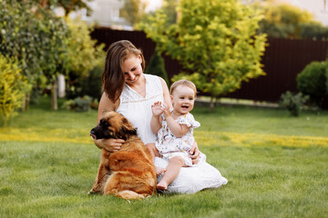 Family day, mother's day. Beautiful smiling young mom and baby daughter cuddling happy domestic dog on the backyard lawn.Mother with child girl are having fun with pet outdoors on summer holiday. - Powered by Adobe