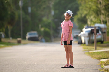 Fototapeta premium Sad moody tired young child girl standing bored alone looking in camera on park alley on sunny summer day