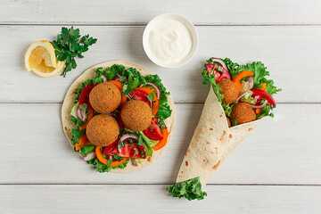 Tortillas, wrapped falafel balls, with fresh vegetables, vegetarian healthy food, on a wooden white background, no people, selective focus.