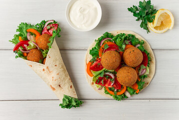 Tortillas, wrapped falafel balls, with fresh vegetables, vegetarian healthy food, on a wooden white background, no people, selective focus.