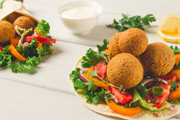 Tortillas, wrapped falafel balls, with fresh vegetables, vegetarian healthy food, on a wooden white background, no people, selective focus.