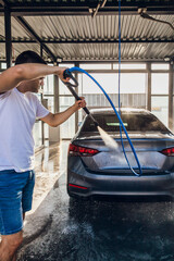 Self-service car wash. A man washes off the foam from his car with water from a pressurized hose at a self-service car wash
