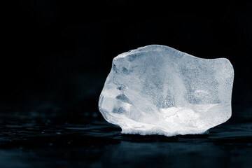 Piece of textured natural ice on a black glossy surface of a winter lake.