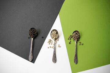 Silver spoons with spices of green, white, black pepper on colorful background