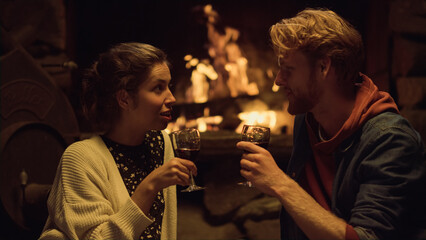 Resting couple drink wine by cozy fireplace. Happy lovers relax in country house