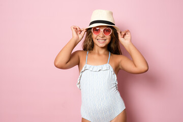 Happy cute beautiful charming little girl in a straw hat and a swimsuit isolated over pink background.