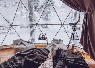 Legs of a man and woman couple in bed against the background of a snow-covered forest in a dome camping.