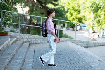 A school student on the steps of the school with a gadget in her hands. Education. Generation Z.