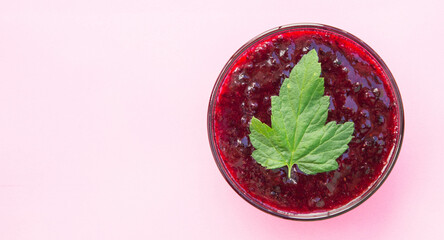 Bowl of homemade currant jam with green leaf on pink background. Top view.
