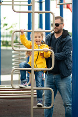 Obraz premium Cute girl with her dad on the sports field. Girl tries to work out on sports simulators and has fun. Childhood. Healthy lifestyle. Family. Conception.