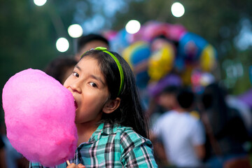 Smiling girl eating cotton Candy at fair. - obrazy, fototapety, plakaty